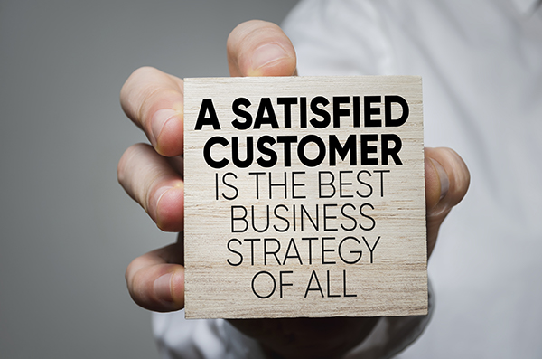 "A satisfied customer is the best business strategy of all" in black font on a block being held by an employee of NCR dealers in NJ